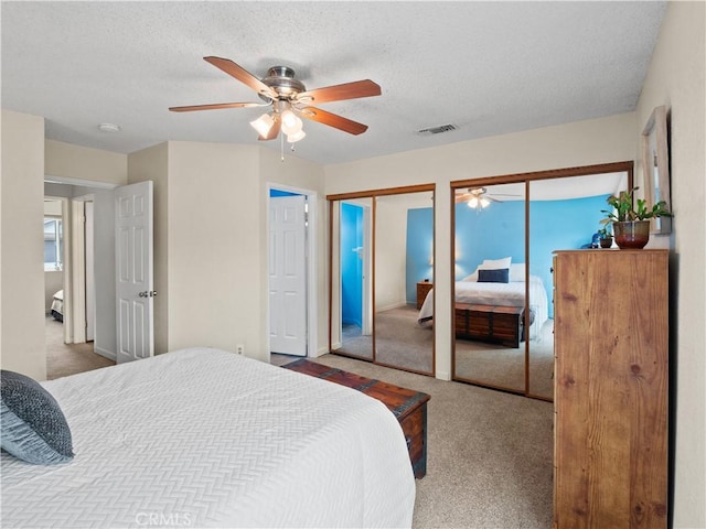 bedroom featuring carpet, visible vents, ceiling fan, multiple closets, and a textured ceiling