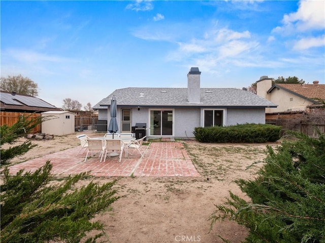 back of house featuring a storage unit, stucco siding, an outbuilding, a patio, and a fenced backyard