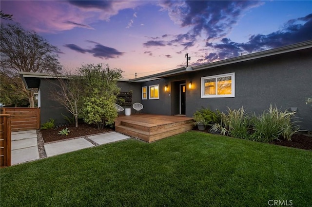 rear view of property with a wooden deck, a yard, and stucco siding