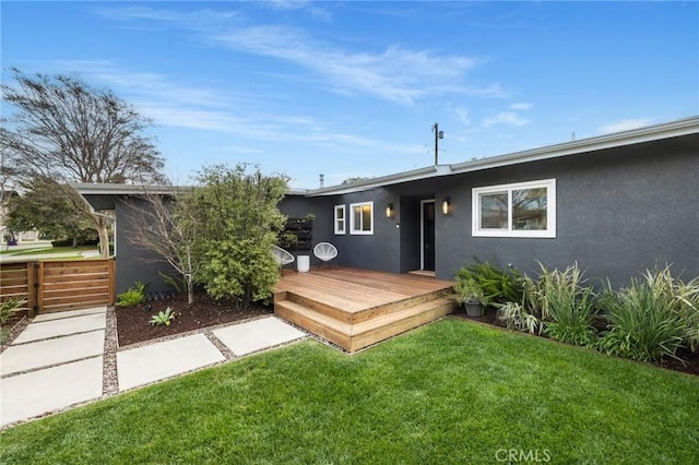 back of house with stucco siding, a yard, and a wooden deck