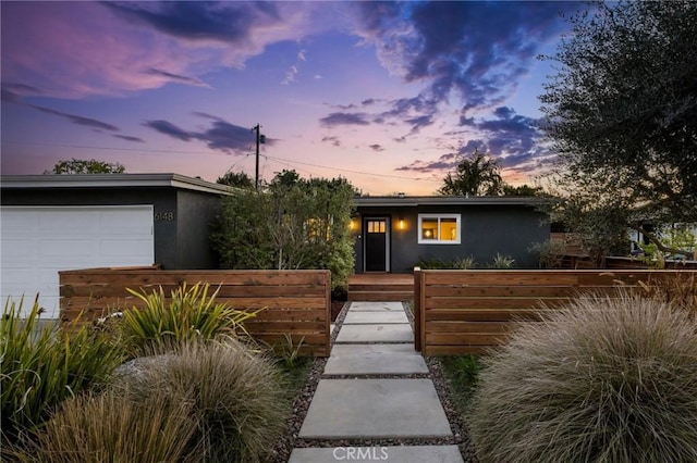 mid-century inspired home featuring stucco siding, a garage, and a fenced front yard