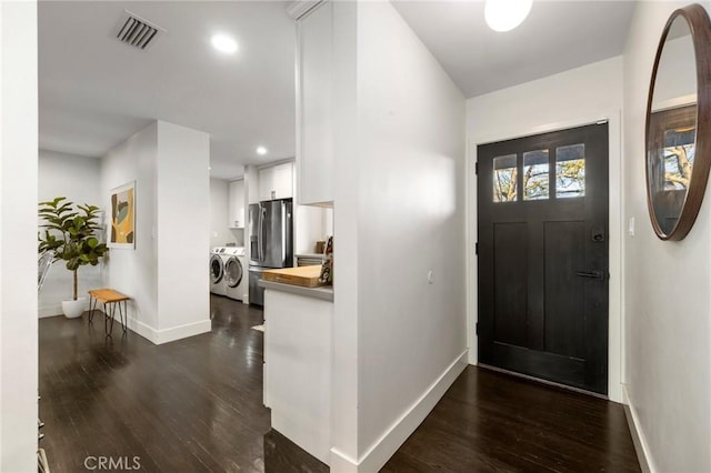 foyer entrance with washer and dryer, dark wood-type flooring, baseboards, and visible vents