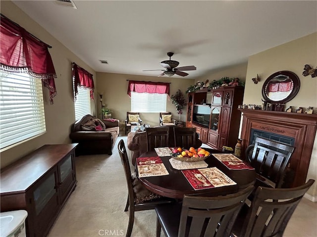 dining area featuring visible vents, light carpet, a glass covered fireplace, and a ceiling fan