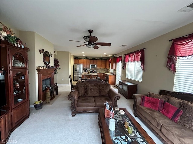 living room featuring visible vents, light carpet, ceiling fan, and a fireplace with flush hearth