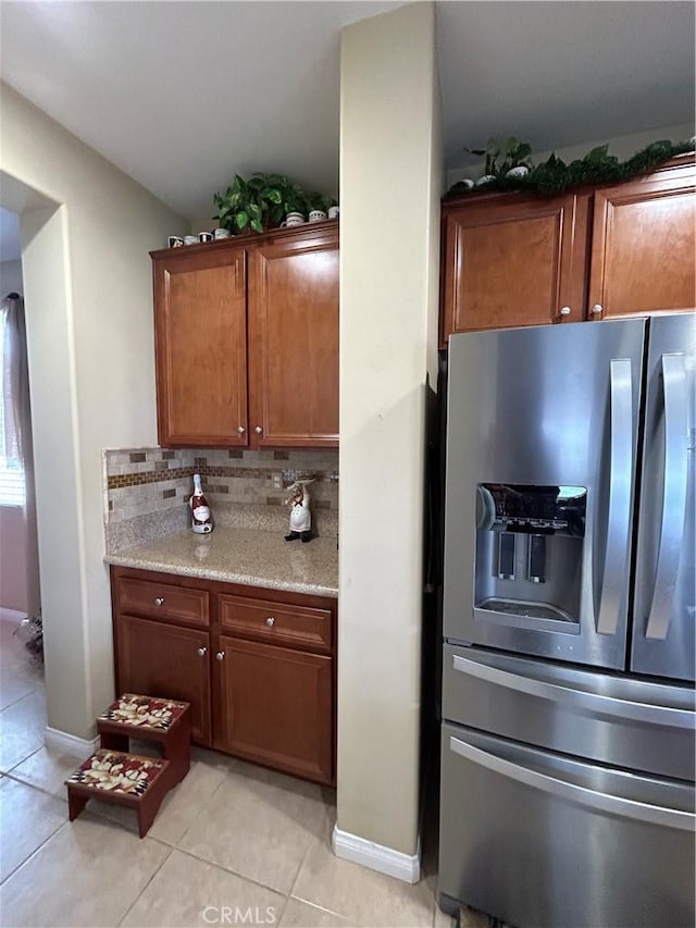 kitchen featuring backsplash, light countertops, light tile patterned flooring, brown cabinetry, and stainless steel fridge