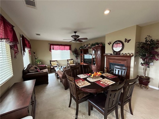 dining room featuring a glass covered fireplace, light colored carpet, visible vents, and ceiling fan