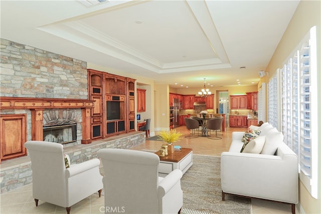 living room with light tile patterned floors, a stone fireplace, crown molding, and a tray ceiling