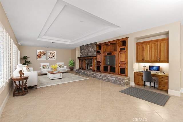 living room featuring built in desk, baseboards, light tile patterned flooring, a fireplace, and a raised ceiling