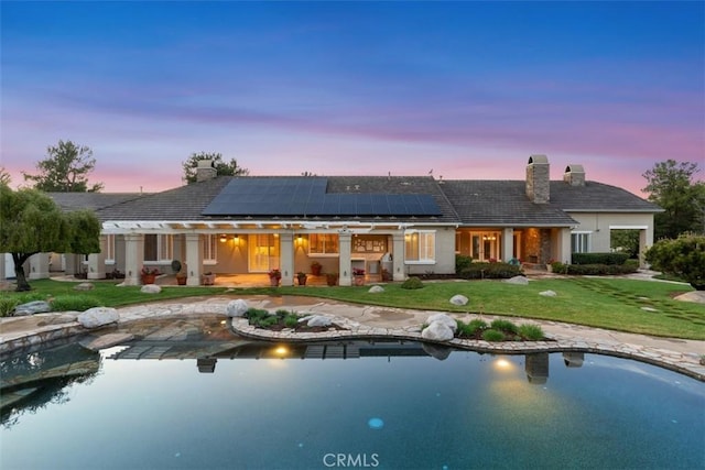 back of property with a lawn, roof mounted solar panels, and a chimney