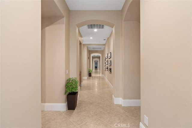 hallway featuring light tile patterned floors, baseboards, arched walkways, and visible vents