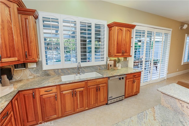 kitchen with stainless steel dishwasher, decorative backsplash, light stone counters, and a sink