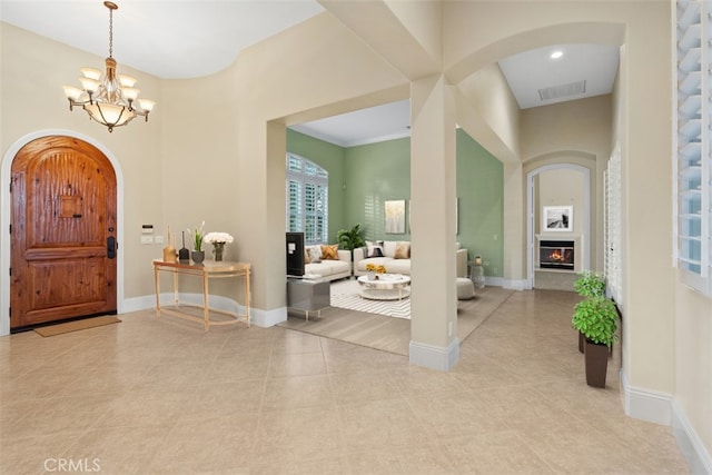 foyer featuring visible vents, baseboards, a chandelier, arched walkways, and a glass covered fireplace