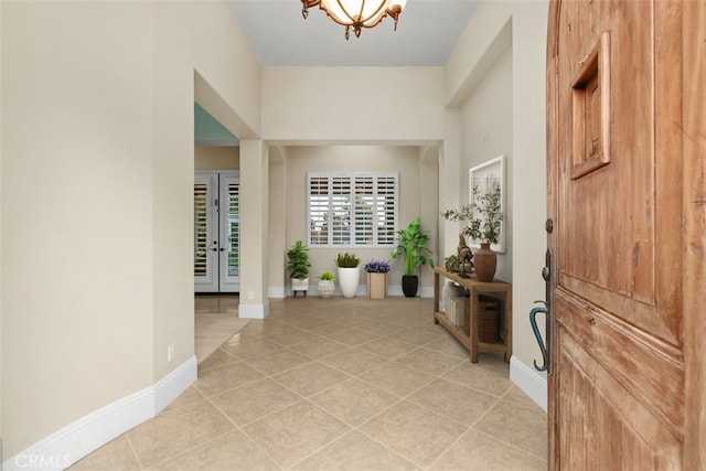 entryway with a notable chandelier, light tile patterned flooring, and baseboards