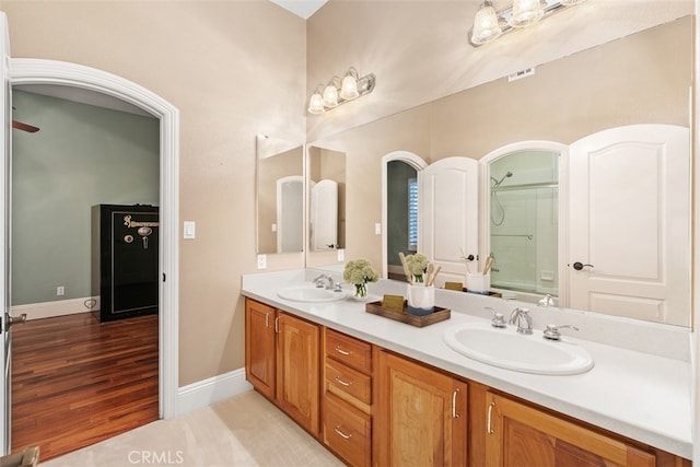 bathroom featuring double vanity, baseboards, a shower with shower door, and a sink