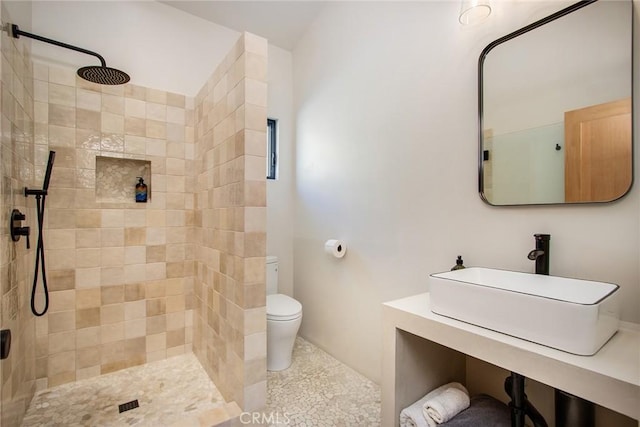 full bathroom featuring a tile shower, toilet, and a sink