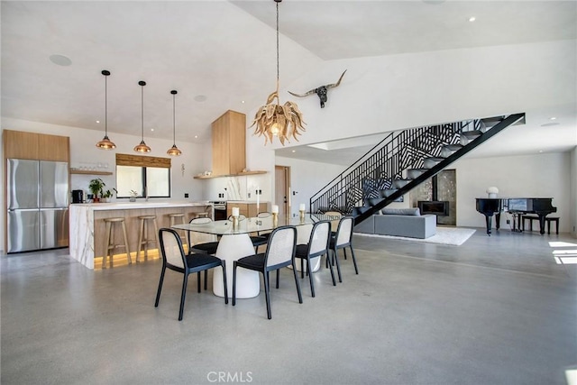 dining area featuring high vaulted ceiling, stairs, and finished concrete flooring