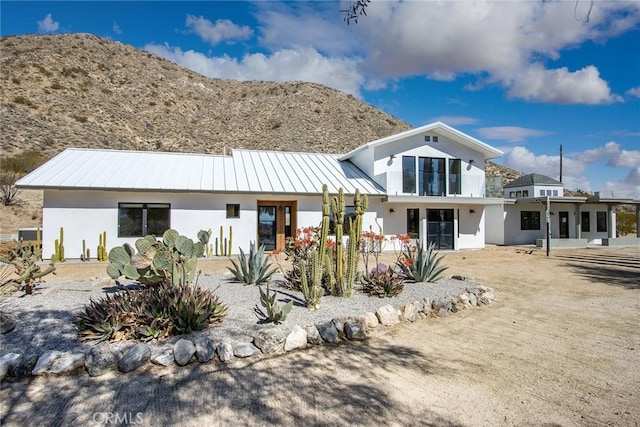 view of front of property featuring stucco siding, a standing seam roof, metal roof, a balcony, and a patio area