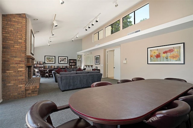 carpeted dining space with visible vents, high vaulted ceiling, a brick fireplace, and rail lighting