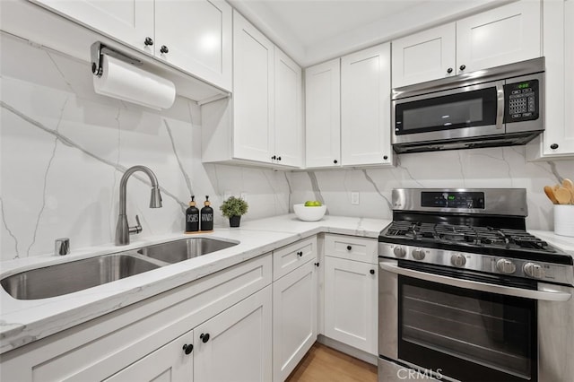 kitchen with tasteful backsplash, light stone countertops, white cabinets, stainless steel appliances, and a sink