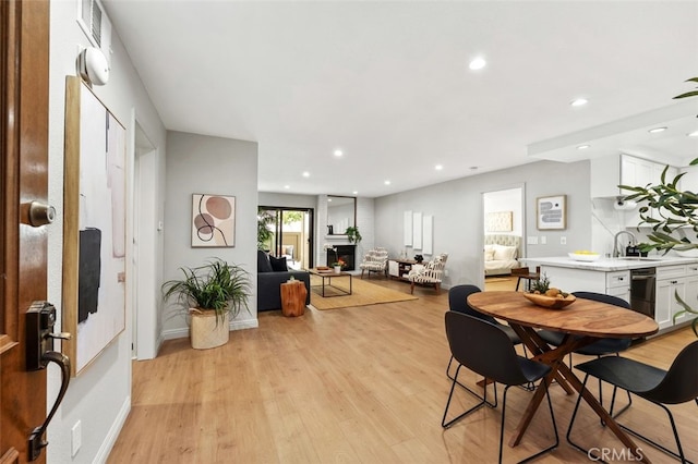 dining area with recessed lighting, baseboards, a lit fireplace, and light wood-style flooring