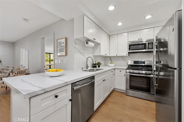 kitchen with light wood finished floors, a peninsula, a sink, stainless steel appliances, and white cabinetry