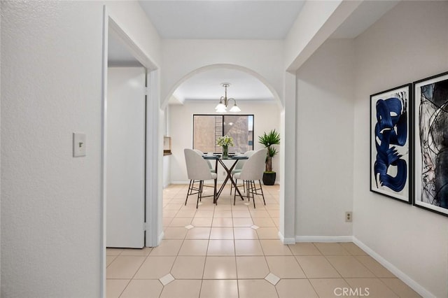 interior space featuring light tile patterned floors, baseboards, arched walkways, and a chandelier