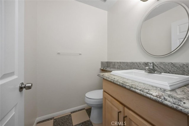 half bath with baseboards, toilet, and vanity