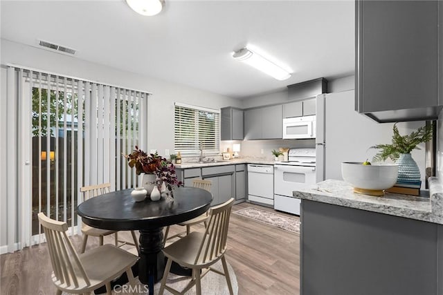 kitchen featuring white appliances, gray cabinets, light wood finished floors, and a sink