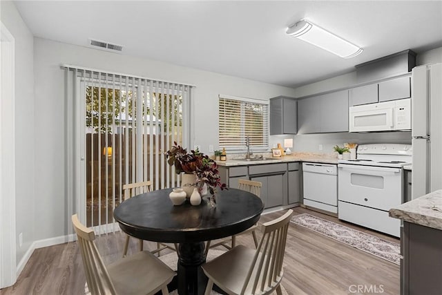 kitchen featuring visible vents, gray cabinetry, light wood-style flooring, white appliances, and a sink