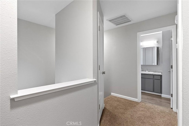 hall featuring a sink, visible vents, baseboards, and carpet flooring