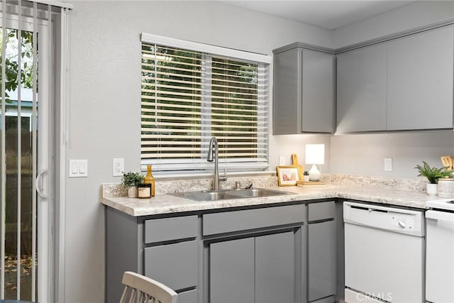 kitchen featuring a sink, dishwasher, gray cabinets, and light countertops