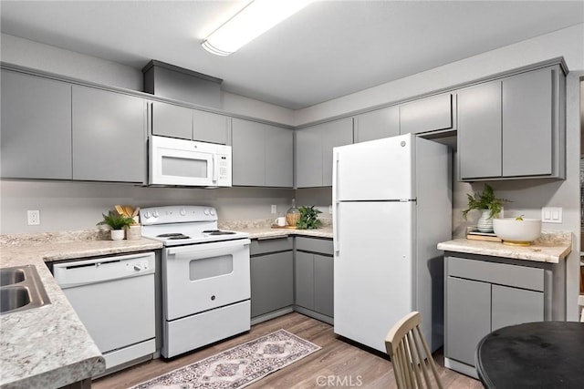 kitchen featuring white appliances, gray cabinetry, light countertops, and light wood finished floors