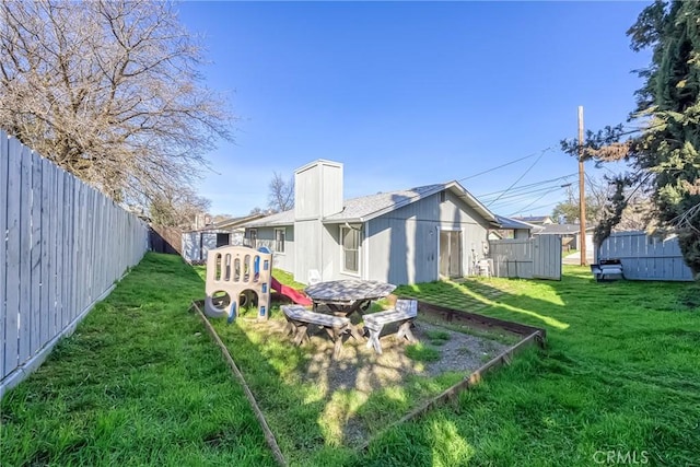 rear view of property featuring a lawn, a fenced backyard, a chimney, and a playground