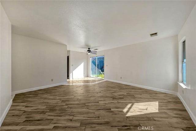 unfurnished room with ceiling fan, visible vents, baseboards, and wood finished floors