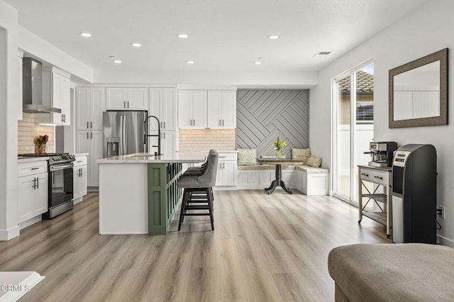 3012 Dunkirk Dr, Oxnard, CA 93035 - kitchen with light wood-style flooring, white cabinets, stainless steel appliances, and wall chimney exhaust hood