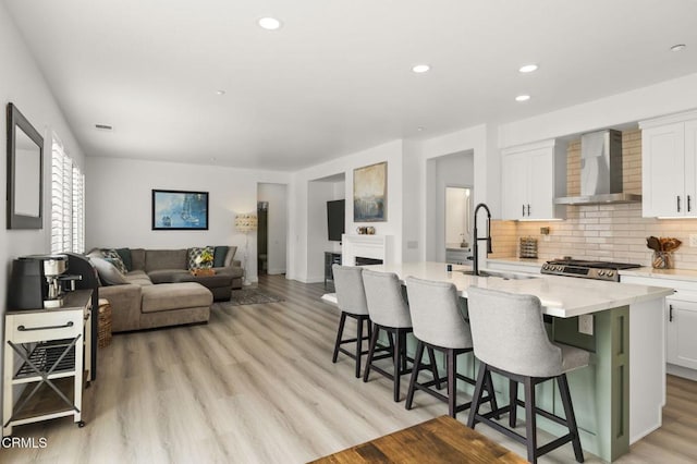3012 Dunkirk Dr, Oxnard, CA 93035 - kitchen featuring a sink, white cabinets, light wood-style floors, wall chimney range hood, and tasteful backsplash