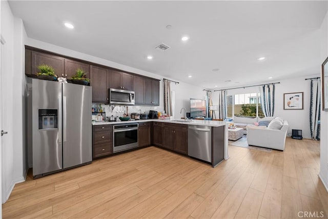 kitchen featuring visible vents, open floor plan, stainless steel appliances, dark brown cabinetry, and light countertops