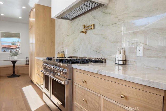 kitchen with tasteful backsplash, ventilation hood, range with two ovens, light stone counters, and light wood-style floors