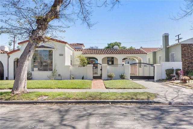 mediterranean / spanish home featuring stucco siding, driveway, a gate, a fenced front yard, and a tiled roof