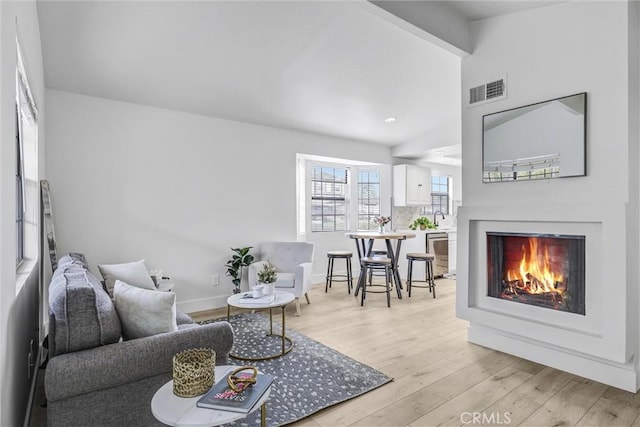 living area with visible vents, light wood-style flooring, a lit fireplace, baseboards, and vaulted ceiling