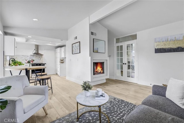 living area featuring visible vents, lofted ceiling, a lit fireplace, french doors, and light wood-type flooring