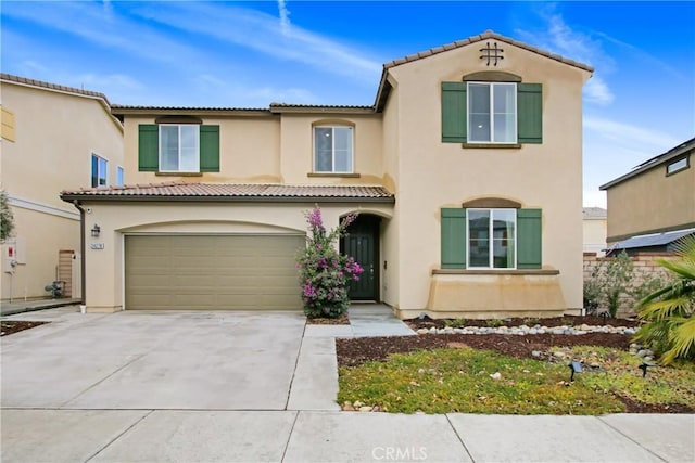 mediterranean / spanish home with a tile roof, stucco siding, an attached garage, and concrete driveway