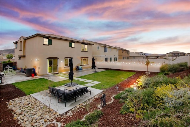 back of house at dusk featuring stucco siding, a patio, a yard, and fence