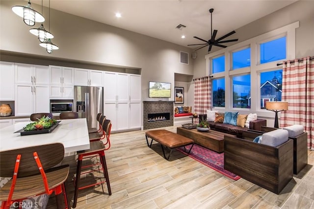 living room featuring light wood finished floors, visible vents, a fireplace, and a high ceiling