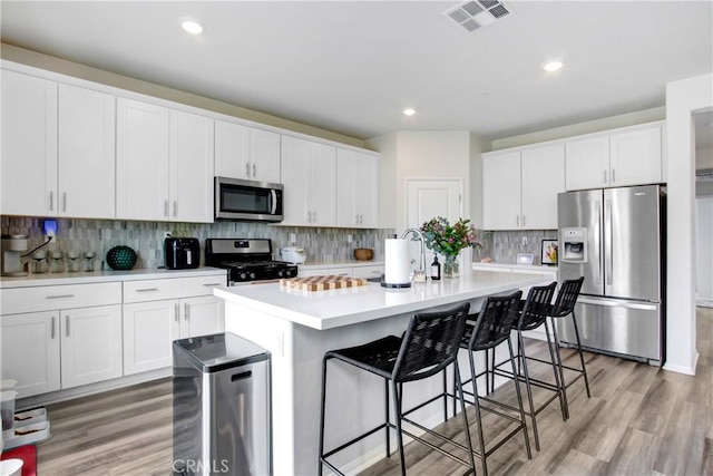 kitchen featuring visible vents, a center island with sink, appliances with stainless steel finishes, white cabinets, and light countertops