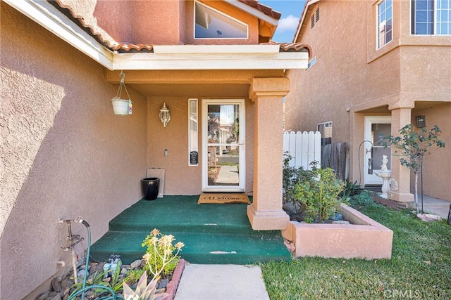 doorway to property featuring a tiled roof, fence, and stucco siding