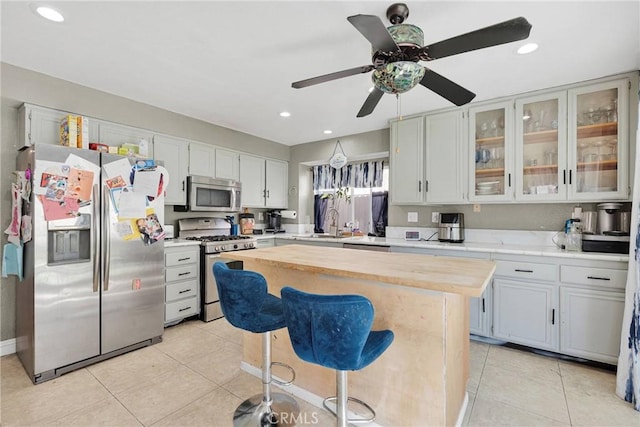 kitchen featuring light tile patterned floors, a kitchen island, butcher block countertops, stainless steel appliances, and glass insert cabinets