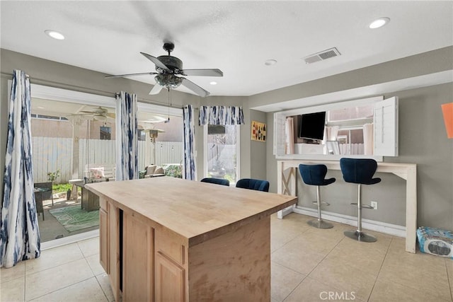 kitchen with light tile patterned floors, a ceiling fan, visible vents, wood counters, and a center island