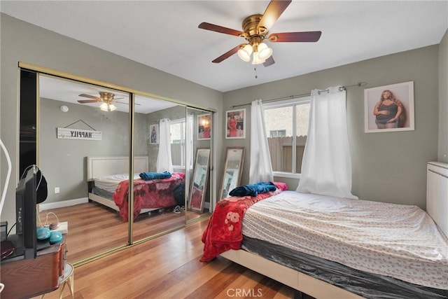 bedroom featuring a closet, multiple windows, baseboards, and light wood finished floors