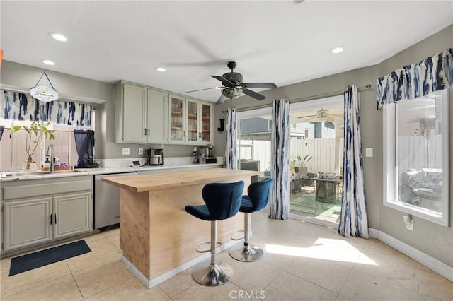 kitchen featuring a breakfast bar area, light tile patterned floors, a sink, wood counters, and stainless steel dishwasher